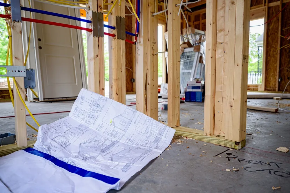 Open wall framing with colored supply lines and building plans on the floor
